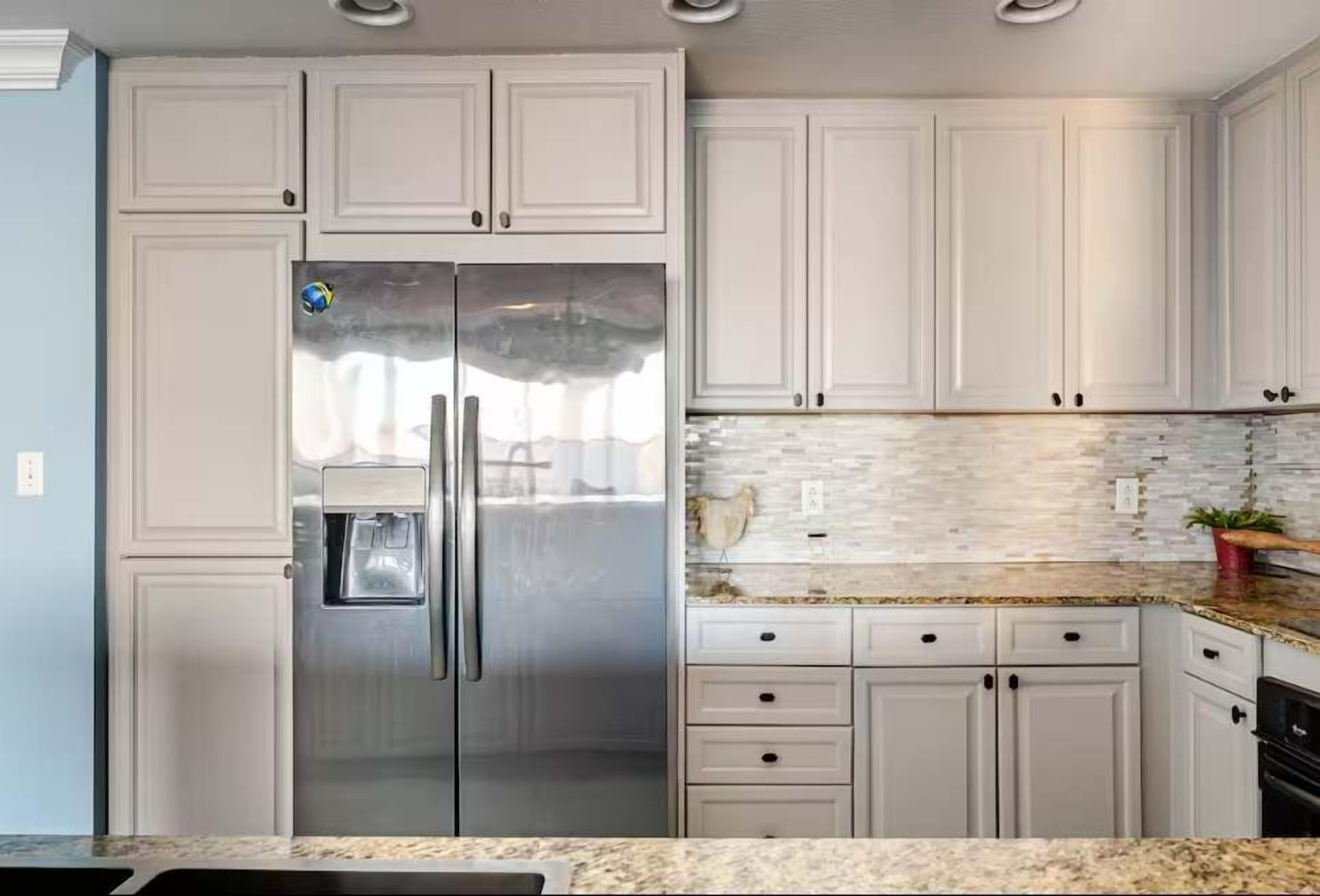 Una cocina con armarios blancos, un refrigerador de acero inoxidable, salpicadero de azulejos y encimeras de granito.