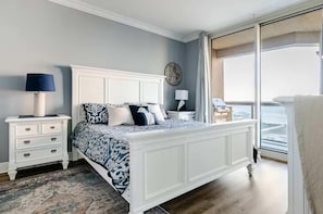 A bedroom with a large bed, a nightstand, a lamp, and a view of the ocean. - Ocean Front Condo w/ Pools, Sauna, Tennis & Gym (Escambia County)