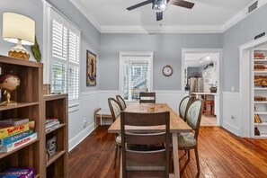 A dining area with a wooden table and chairs, a ceiling fan, and a bookshelf with board games. - Perfect location! Huge, historic & updated home, easy stroll to downtown St. Aug (St. Augustine)