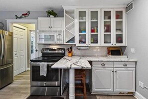 A kitchen with white cabinetry, a marble countertop, stainless steel appliances, and a small island with stools. - Perfect location! Huge, historic & updated home, easy stroll to downtown St. Aug (St. Augustine)