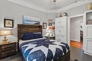 A bedroom with a bed, nightstands, a wooden headboard, a wall-mounted artwork, and a closet with white doors. - Perfect location! Huge, historic & updated home, easy stroll to downtown St. Aug (St. Augustine)