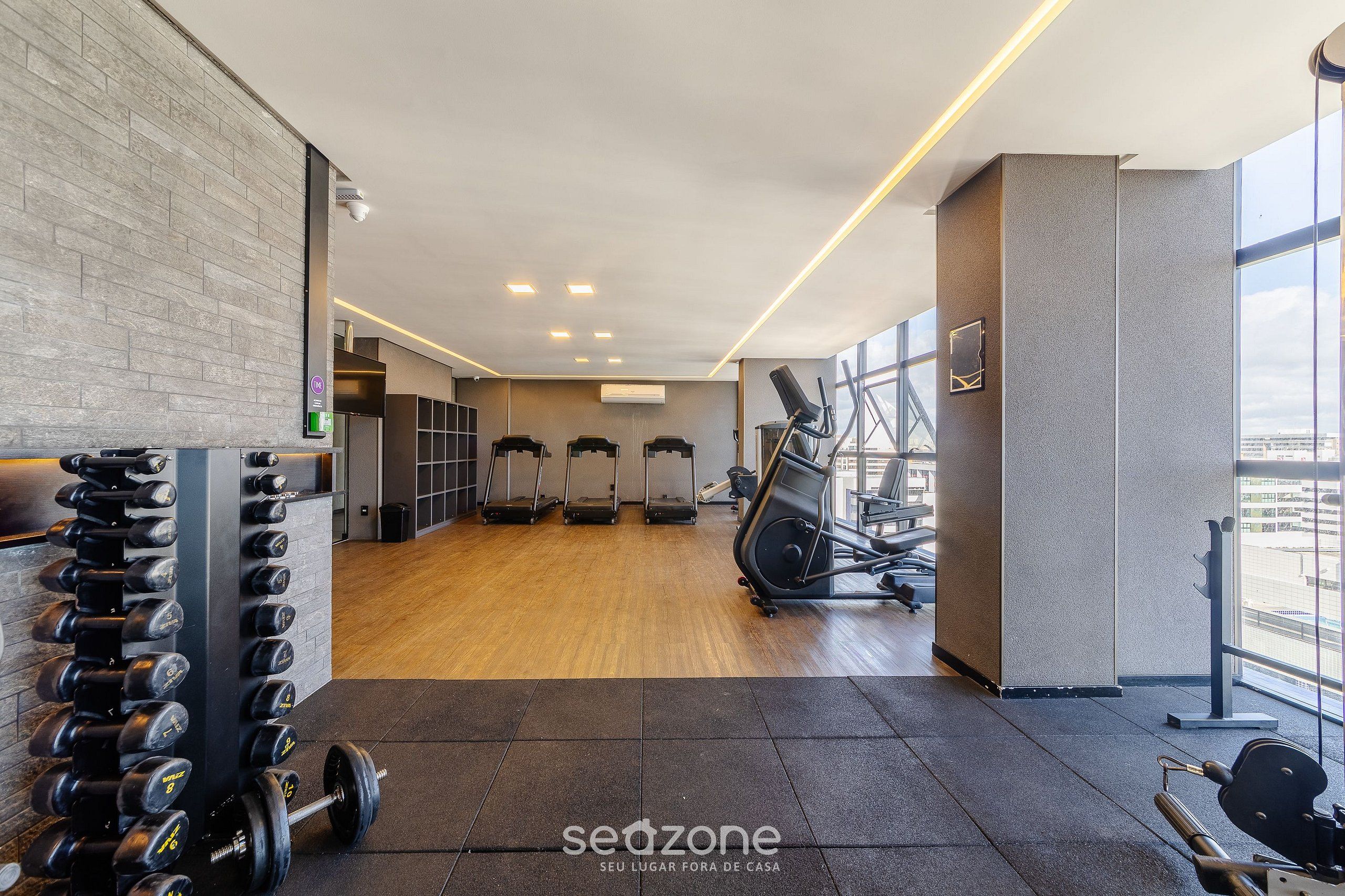 Un gimnasio con equipo de levantamiento de pesas, cintas de correr y un ventanal grande.