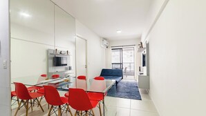 Habitació moderna i ben il·luminada amb taula de vidre, cadires vermelles, un sofà i televisió penjada a la paret.