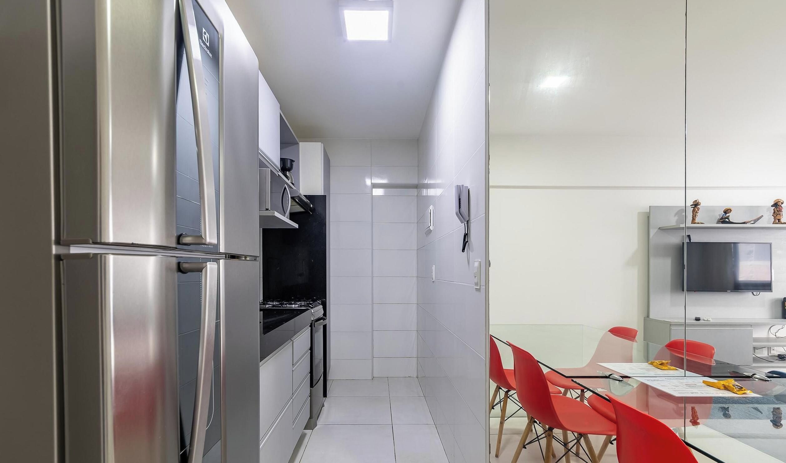 Cocina compacta con refrigerador, estufa y microondas, que da paso a un comedor con sillas rojas y una mesa.