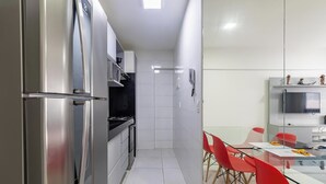 Cuina compacta amb nevera, fogó i microones, que dona a una zona de dinar amb cadires vermelles i taula.