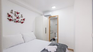 A bedroom with a bed, a wall-mounted decorative piece, a wardrobe, and a bathroom visible through an open door. - Apt in Condo w/ Pool in Federacao Hfo1006 (Salvador)