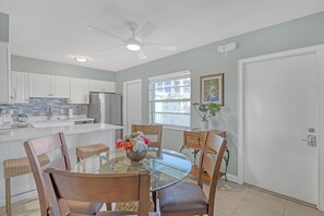 Una cocina moderna con armarios blancos, un refrigerador de acero inoxidable y una mesa de comedor de vidrio con sillas.
