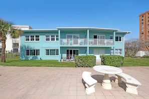 A two-story building with a balcony, a patio with a table and benches, and a well-maintained lawn. - OUTSTANDING Location!  High-end 2/1 On The Beach, Close To The Port & Pier! (Cocoa Beach)