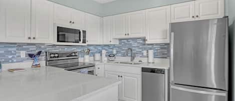 A modern kitchen with white cabinets, stainless steel appliances, and a blue-tiled backsplash.