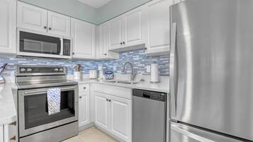 Cozinha moderna com eletrodomésticos de aço inoxidável, armários brancos e painel de azulejos azuis.