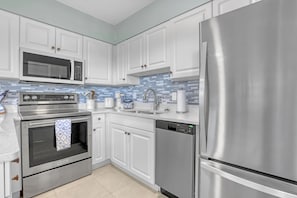 A modern kitchen with stainless steel appliances, white cabinetry, and a blue-tiled backsplash.