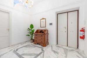 A hallway with a marble floor, a wooden dresser, a potted plant, a mirror, and a fire extinguisher. - Authentic Prati Penthouse (Rome)
