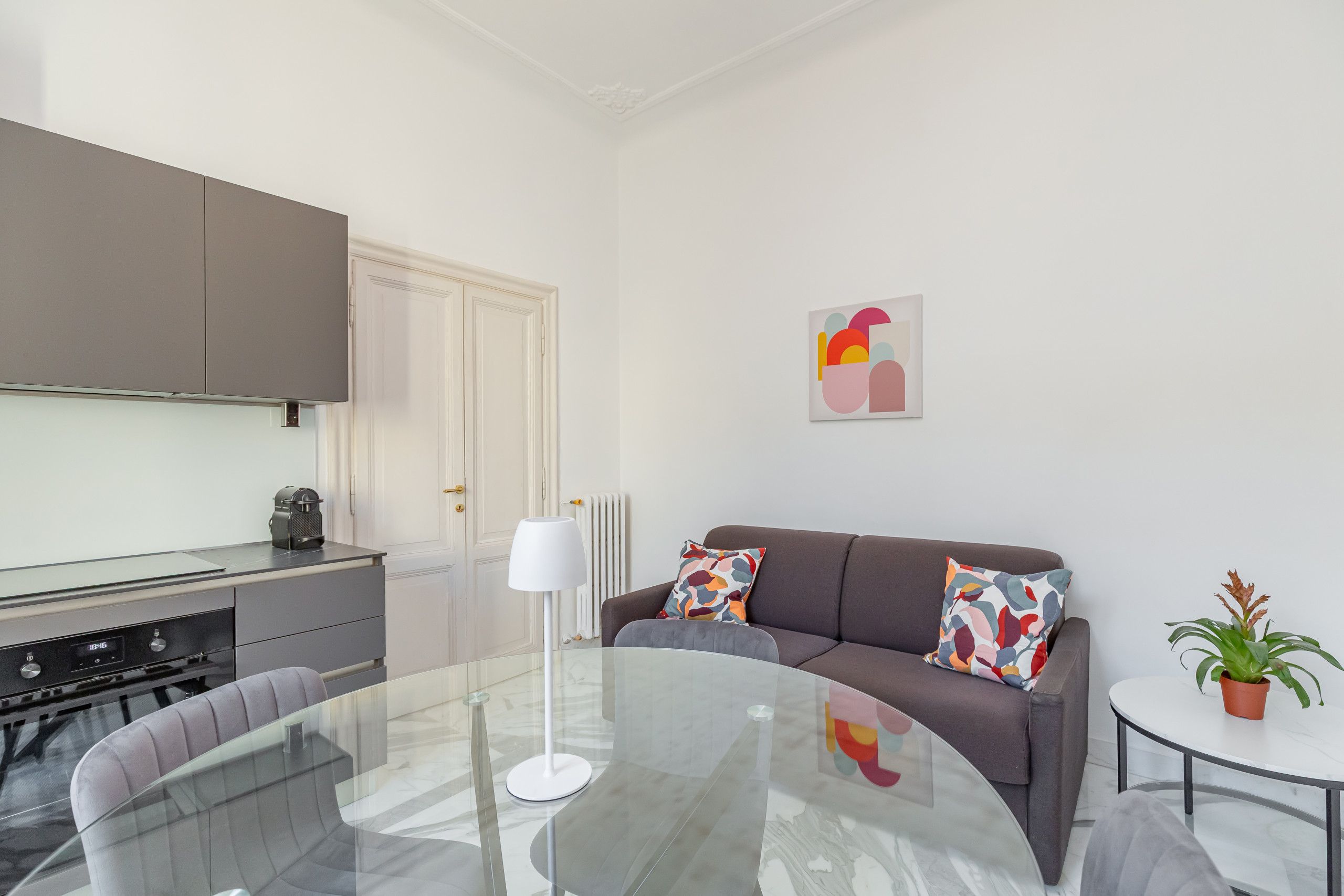 Una sala moderna con una mesa de vidrio, un sofá gris y una mesita redonda con una planta en maceta.