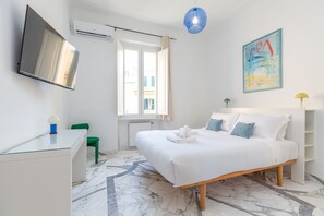A modern hotel room with a bed, a desk, a chair, a TV, and a window with curtains. - Authentic Prati Penthouse (Rome)