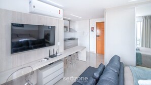 Een moderne woonkamer met een flatscreen televisie, een keukenhoek en een bank.