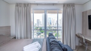 Een hotelkamer met een bed, een bank, een televisie en een stadszicht door grote ramen.