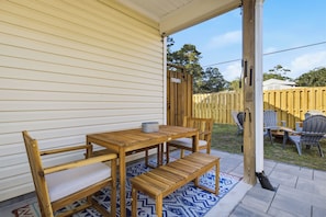 Eine Holzterrasse mit Tisch und Stühlen, einem Teppich und einem Holzzaun im Hintergrund.