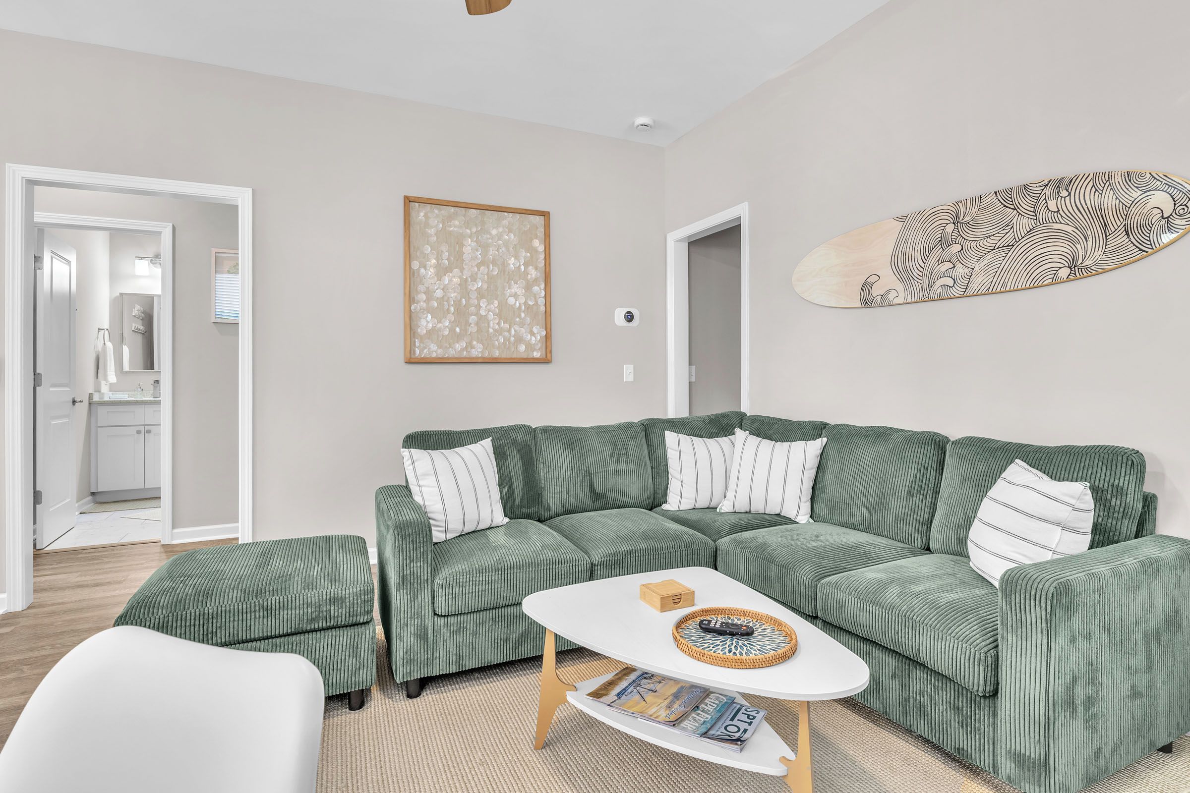 A modern living room with a green sofa, a white coffee table, and a decorative surfboard.