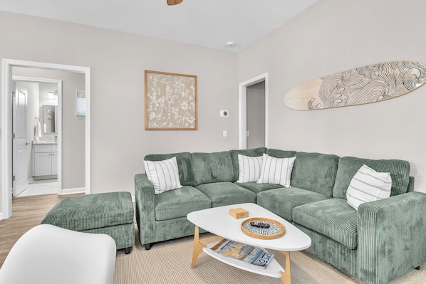 Ein modernes Wohnzimmer mit einem grünen Sofa, einem weißen Couchtisch und einem dekorativen Surfbrett.
