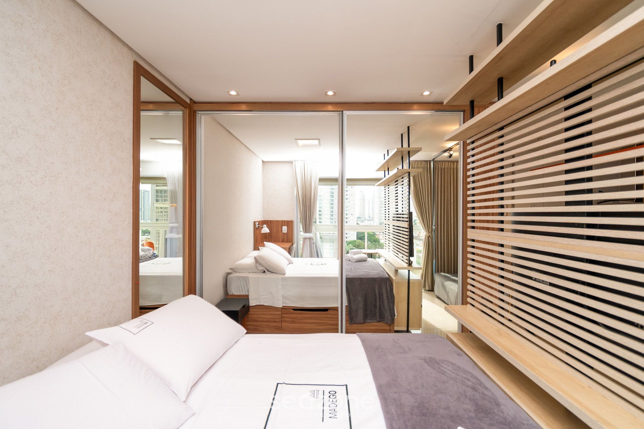 A modern hotel room with a large bed, a wooden wardrobe, and a view of the city through the window.