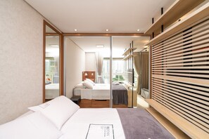 Una habitació d'hotel moderna amb un llit gran, un armari de fusta i vista a la ciutat per la finestra.