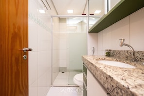 A bathroom with a wooden door, a glass shower enclosure, a white toilet, and a granite countertop with a sink and mirror. - Flat in Full Condo, Setor Bueno - Txp0903 (Goiânia)