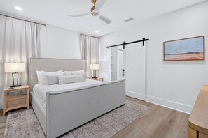 Un dormitorio moderno con una cama grande, lámparas de noche, ventilador de techo, armario corredero y un cuadro en la pared.