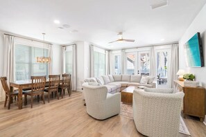 A modern living room with a sectional sofa, a dining table with chairs, and a ceiling fan.