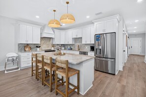 A modern kitchen with white cabinets, a stainless steel refrigerator, and a central island with bar stools.
