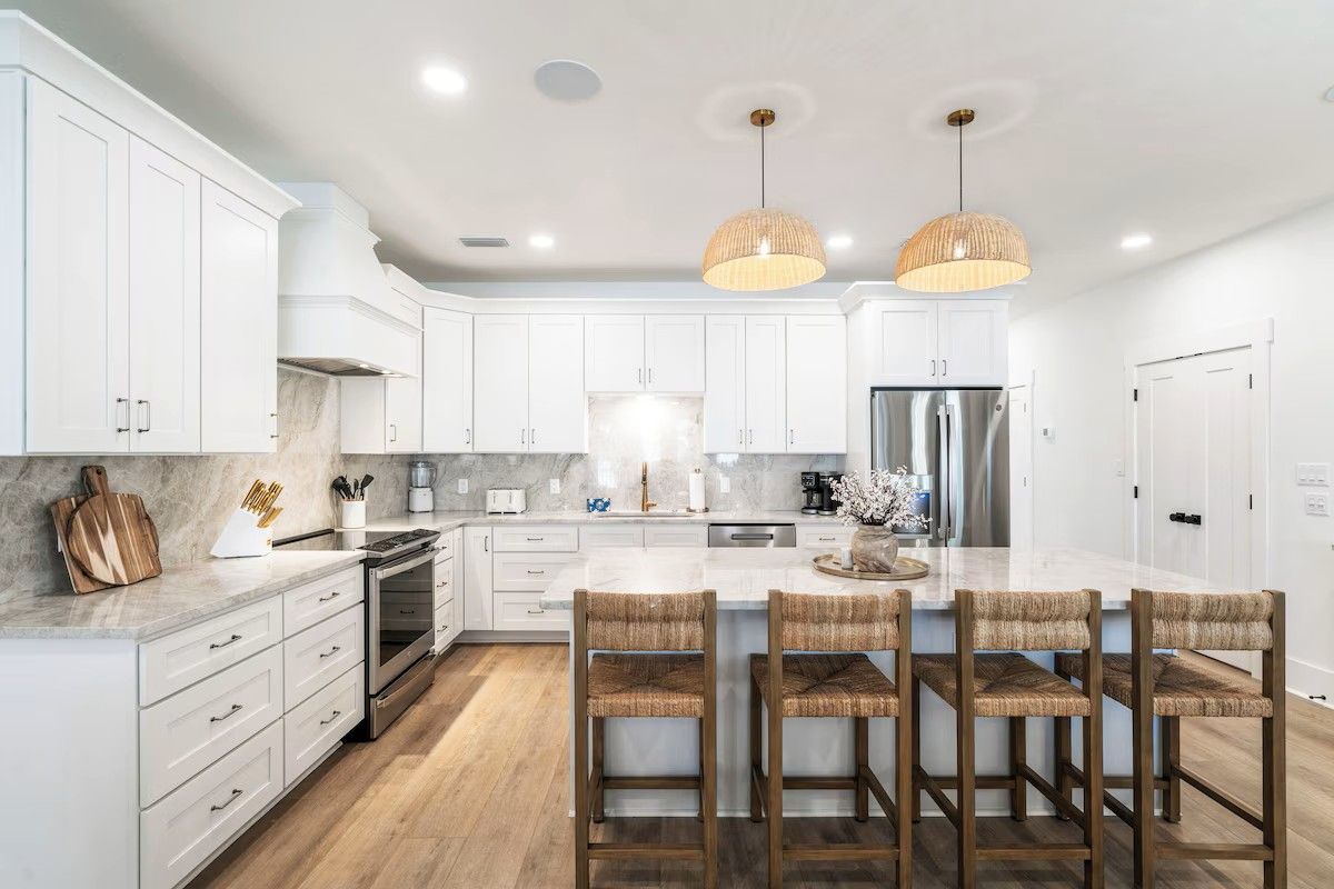 Una cocina moderna con armarios blancos, una isla central con taburetes de bar, electrodomésticos de acero inoxidable e iluminación colgante.