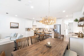 A modern kitchen with white cabinetry, a wooden dining table, and a chandelier.