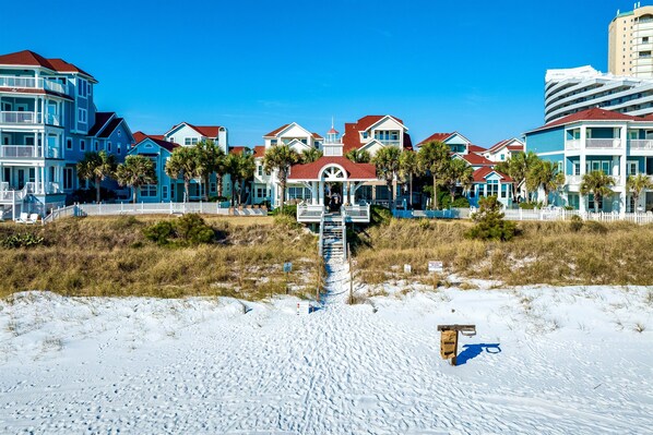 A beachfront hotel with a central pavilion, multiple-story buildings, and a sandy beach in the foreground.