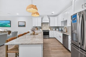 Una cocina moderna con muebles blancos, una isla grande, electrodomésticos de acero inoxidable y una lámpara colgante.