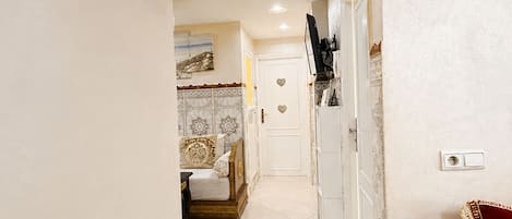 A hallway with a bed, a TV, and a door with a heart-shaped decoration.