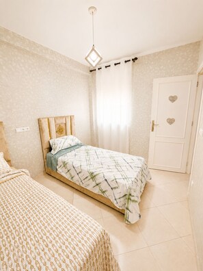 A bedroom with a bed, a bedside table, a door with a heart-shaped decoration, and a hanging light fixture. - Airport Comfort Tanger – Apartment (Tanger)