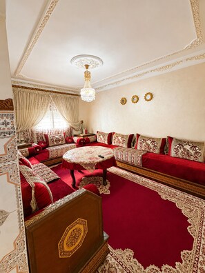 A room with a red carpet, a round table, and a sofa set with patterned cushions. - Airport Comfort Tanger – Apartment (Tanger)