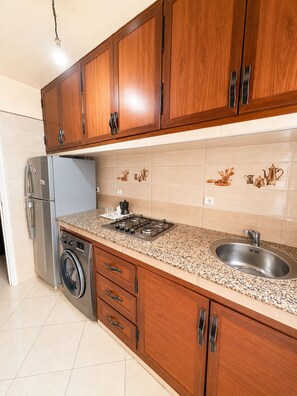 A kitchen with wooden cabinets, a stainless steel sink, a built-in washing machine, and a gas stove. - Airport Comfort Tanger – Apartment (Tanger)