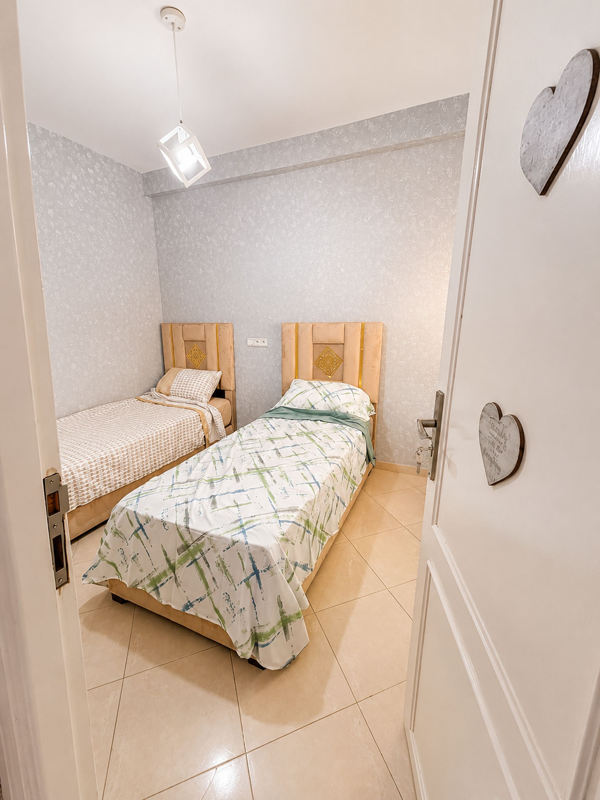 A bedroom with two beds, a light fixture, and a door with a heart-shaped decoration.