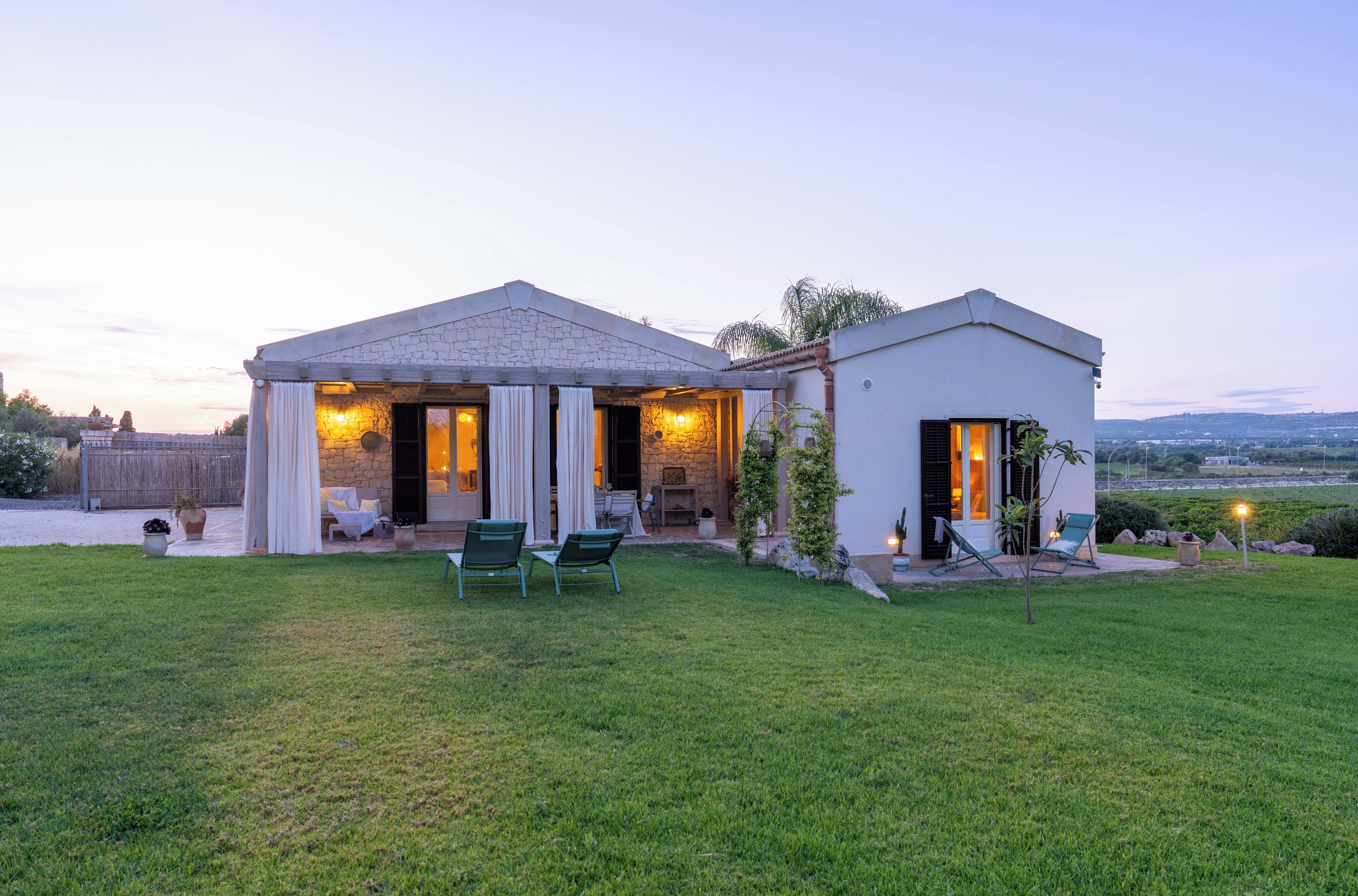 A two-story house with a stone facade, a covered patio with outdoor seating, and a well-maintained lawn.