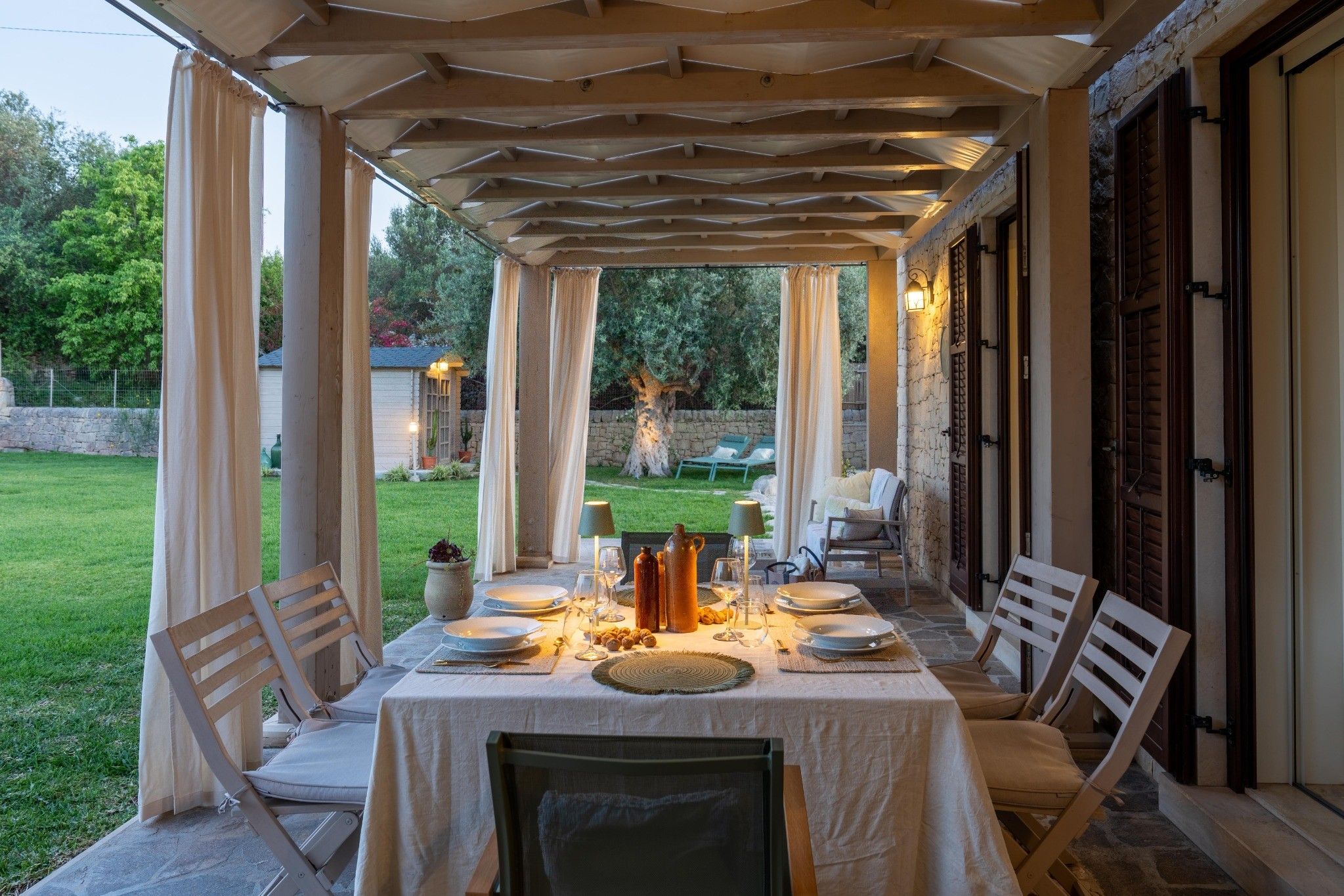 Un espace extérieur aménagé pour les repas, avec une pergola couverte, une table dressée pour quatre personnes et une vue sur le jardin.