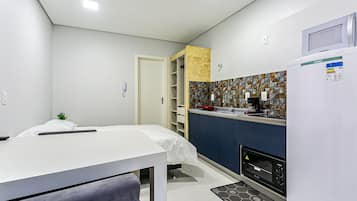 Una habitación compacta con cama, una mesita pequeña, una kitchenette con microondas, horno tostador y refrigerador.