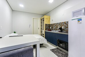 A compact room with a bed, a small table, a kitchenette with a microwave, a toaster oven, and a refrigerator. - Cozy Studio Facing the Lagoon Sdr007 (Florianópolis)