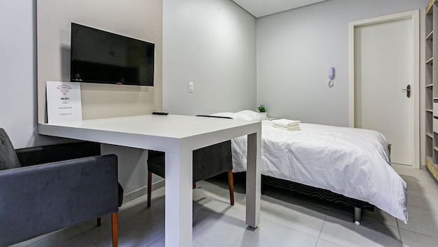 Una camera moderna con una scrivania bianca, un letto con biancheria da letto bianca, una TV a muro e una libreria.