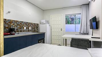 Habitación de hotel compacta con kitchenette, una cama, un escritorio con silla, televisión y ventana con cortinas.