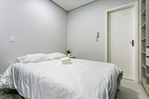 A neatly made bed with white bedding, a bedside table with a plant, and a closed door. - Cozy Studio Facing the Lagoon Sdr007 (Florianópolis)