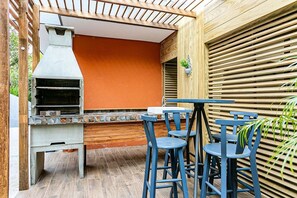 An outdoor patio with a barbecue grill, a table, and blue chairs. - Cozy Studio Facing the Lagoon Sdr007 (Florianópolis)