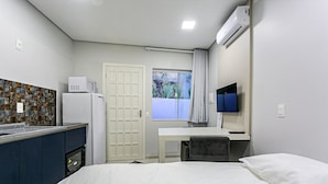 Una camera d'albergo compatta con un letto, una scrivania, una TV, un forno a microonde e un angolo cottura.