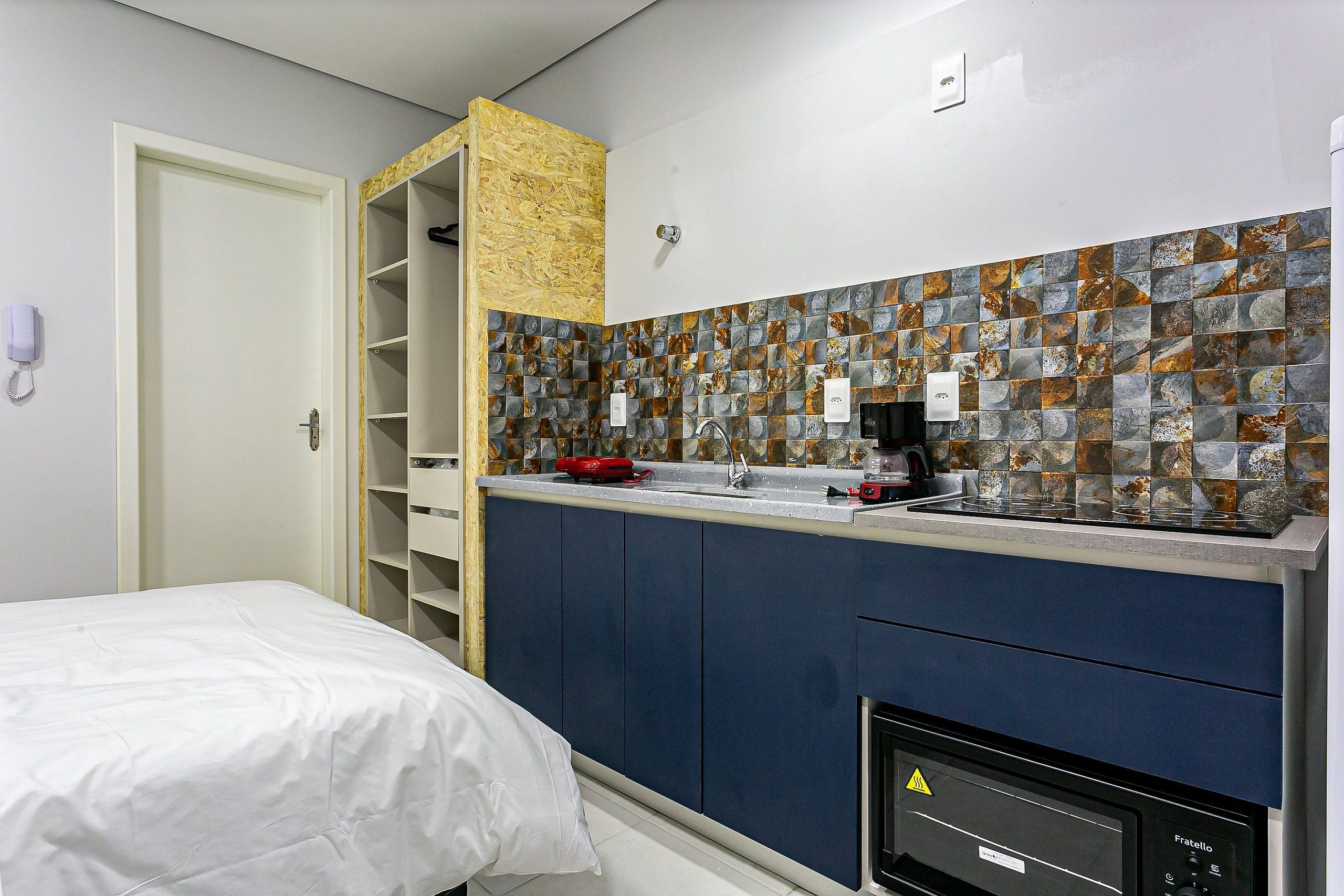 Una habitación de hotel compacta con una cama, una kitchenette con estufa y un baño con ducha.