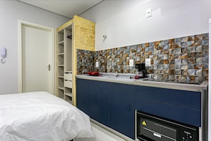 A compact hotel room with a bed, a kitchenette with a stove, and a bathroom with a shower. - Cozy Studio Facing the Lagoon Sdr007 (Florianópolis)