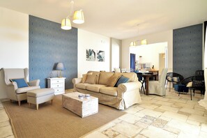 Un salon comprenant un canapé, un fauteuil, un pouf et une table basse. Il y a également un coin repas avec une table et des chaises.